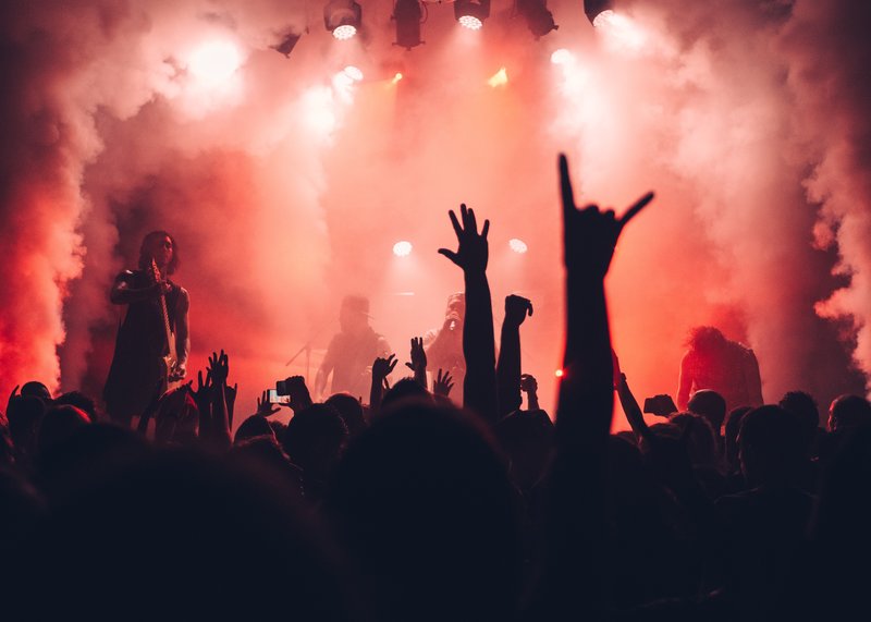 A silhouetted crowd at a rock concert. The stage is lit up with red lighting, the musicians are blurred out by the dry ice.