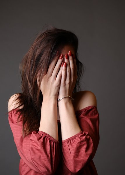 A brunette woman hiding her face behind her hands